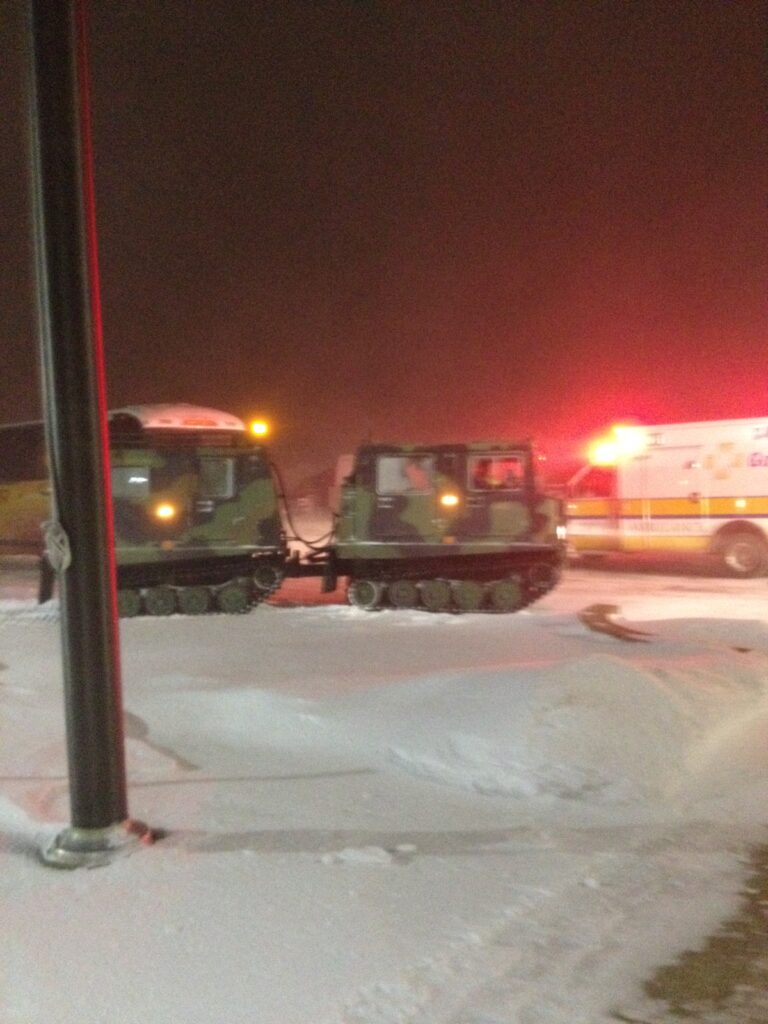 Tracked vehicles and an ambulance moving through the snow at night